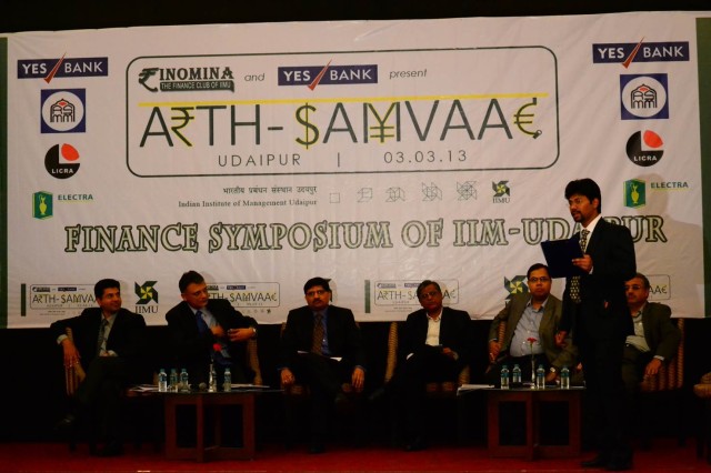 Panel discussion at Arth-Samvaad 2013 being conducted by Abhinandan Ghosh(standing), student at IIM Udaipur. Panelists include (seated from left to right)  Deepak Doegar, CFO, GE Energy India; Mr. Manish Vora, President & Regional Head – Gujarat, Corporate & Institutional & Infra Banking ; Mr. Nitin Parekh, CFO, Cadilla Healthcare, Mr. Makarand Padalkar, CFO, Oracle Financial Services; Mr. Mahesh Taliyani, Group Financial Controller, Shapoorji Pallonji Group, Prof. Ramesh Bhatt, Former Proff, IIMA and Exec. Chairman W One Management Systems